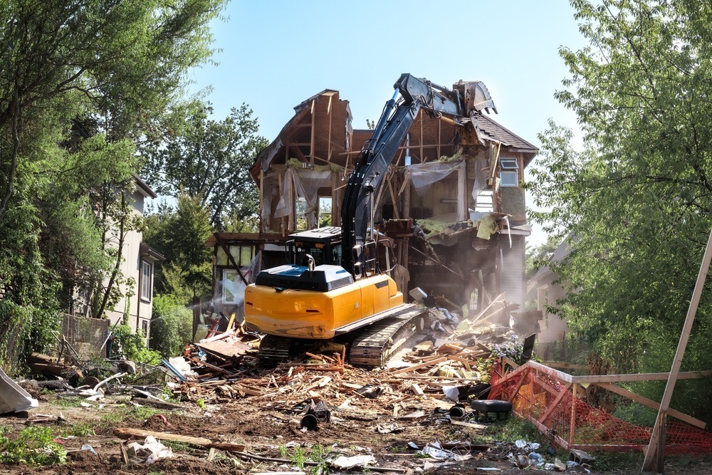 Excavator demolishing a two-story house surrounded by wood and construction debris - Cajun Care Demolition & Tree Service in New Orleans