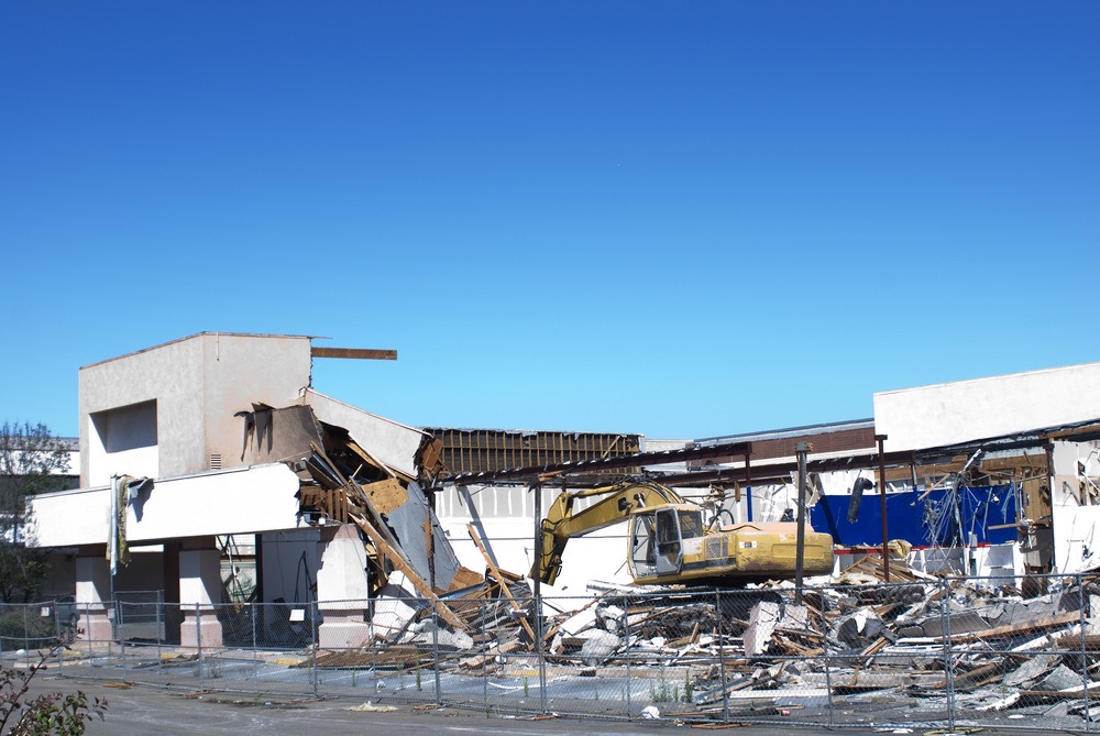 Excavator dismantling a commercial building behind a safety fence - Cajun Care Demolition & Tree Service in New Orleans