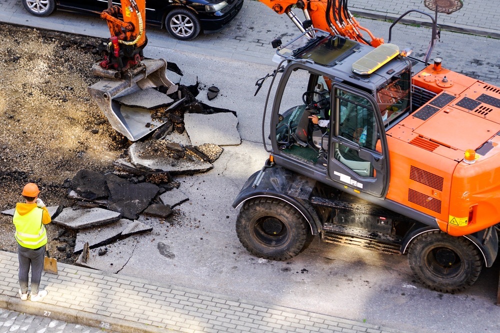 Excavator removing broken asphalt from a road - Cajun Care Demolition & Tree Service in New Orleans