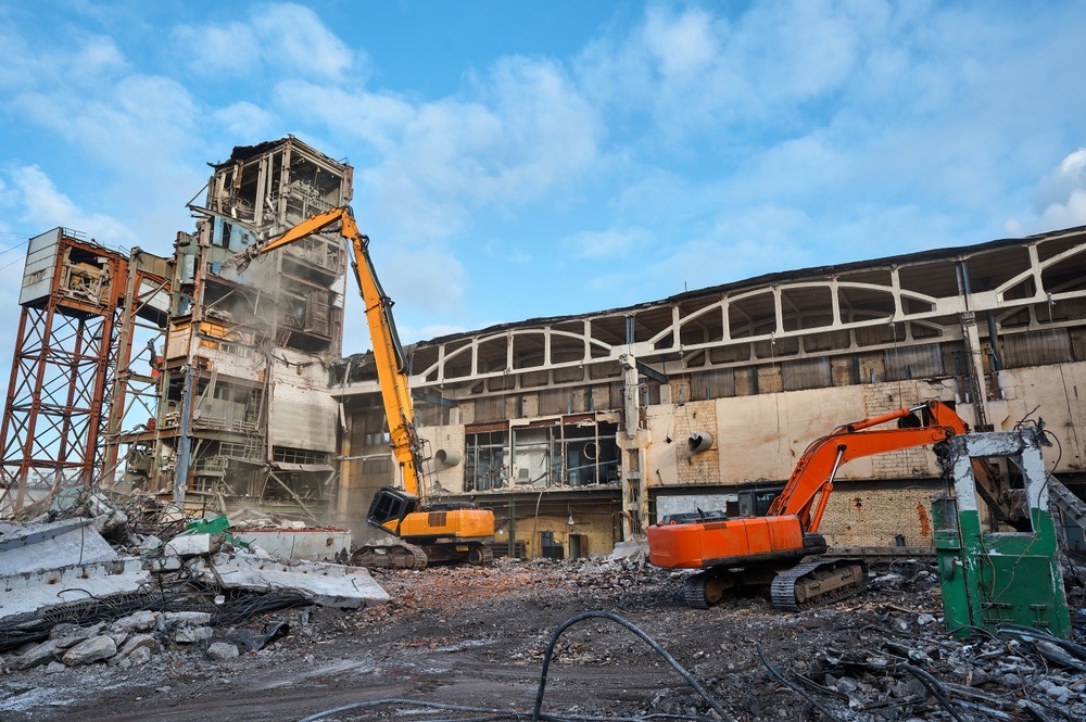 Excavators demolishing an industrial building surrounded by concrete rubble - Cajun Care Demolition & Tree Service in New Orleans