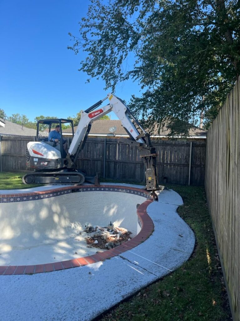 Mini excavator breaking concrete around an empty backyard swimming pool - Cajun Care Demolition & Tree Service in New Orleans