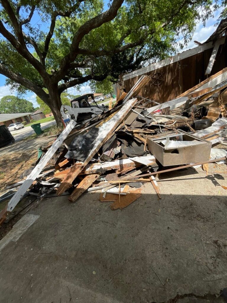 Skid steer beside demolition debris from a partially dismantled wooden structure - Cajun Care Demolition & Tree Service in New Orleans
